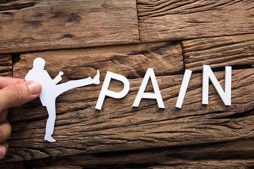 Closeup of hand holding paper businessman kicking word pain on wood, representing pain relief procedures