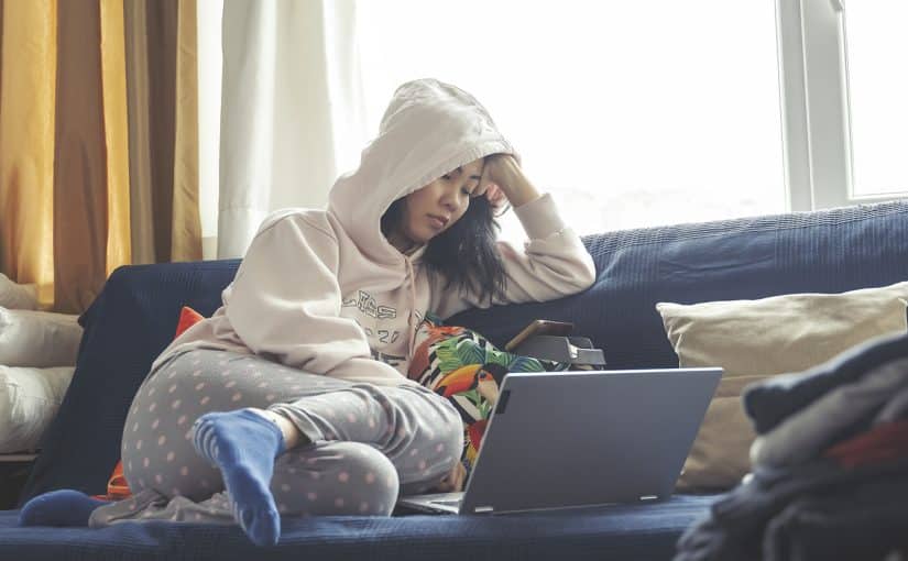 A girl in a hoodie sitting on a couch with her laptop resting.