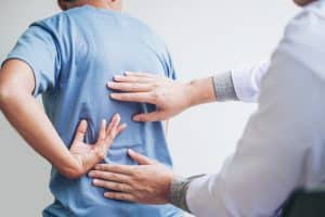 A doctor doing a back examination on a man with a blue shirt.